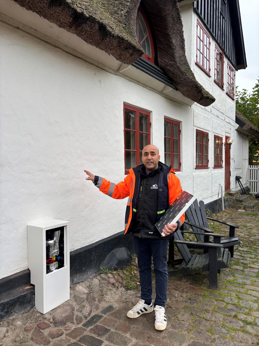 Projektleder for M.J. Erikssons fjernvarmeinstallationer i Lyngby, Hadi Saharabek, forklarer hvordan den fredede ejendom har krævet nogle kreative løsninger, bl.a. den specialbyggede hvide kasse, der er konstrueret, så den passer til hus og sokkel.